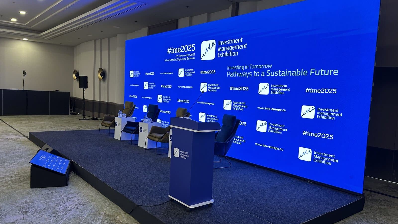 le mur LED de la scène principale portant l'identité de l'événement, avec les sièges du panel et un pupitre