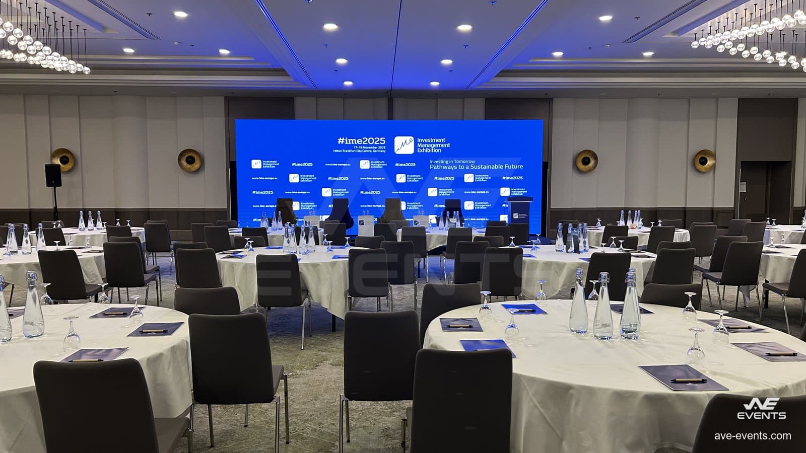 IME Frankfurt 2025: der Ballsaal vor Beginn der Sitzung, mit eingedeckten runden Tischen und der LED-Wand, die das Erscheinungsbild der Konferenz zeigt