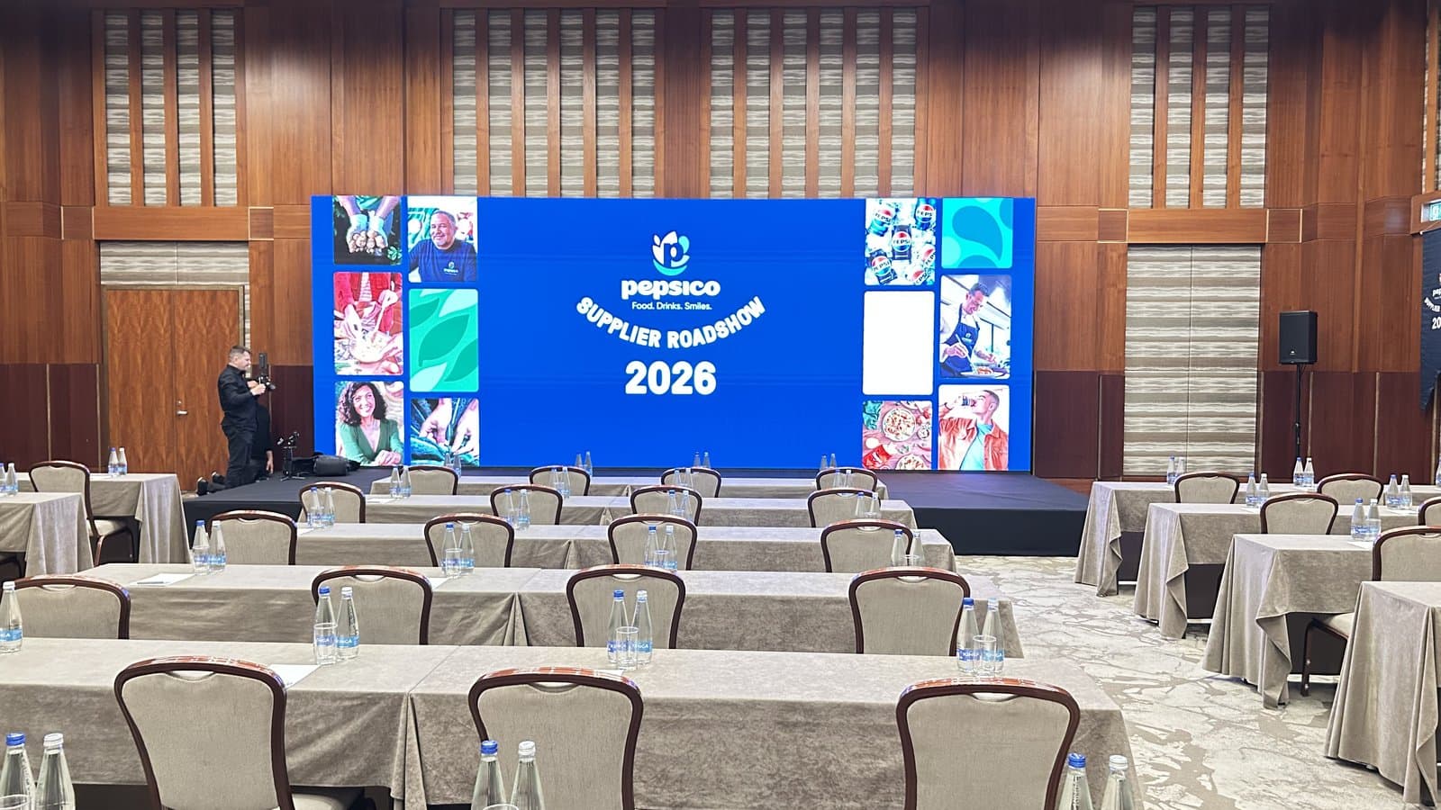 le mur LED de la scène portant l'identité du Supplier Roadshow, avec la salle installée en rangées façon salle de classe